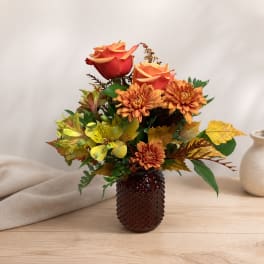 Orange roses and chrysanthemums arranged in a dark vase