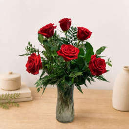 Red roses arranged in a clear glass vase with greenery