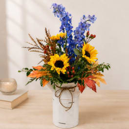 Blue and yellow floral arrangement in a white metal container with a bow