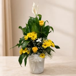 Yellow and white floral arrangement in a white pot with a ribbon