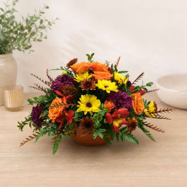 Mixed orange, yellow, and purple flowers in a low bowl arrangement