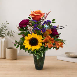Mixed bouquet with a sunflower, roses, and orange alstroemeria in a dark vase