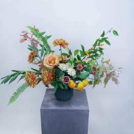 Mixed floral arrangement in a dark vase with peach roses and orange chrysanthemums