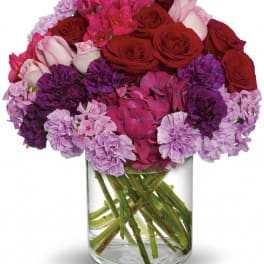 Bouquet of red roses and pink-purple flowers in a clear glass vase