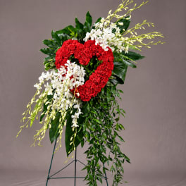 Heart-shaped red floral spray with white orchids and cascading greenery on a stand