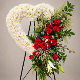 Heart-shaped floral wreath with white chrysanthemums and red roses on a stand