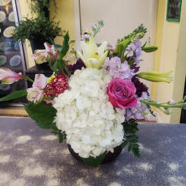 Mixed bouquet with white hydrangea, pink rose, and lilies in a dark vase