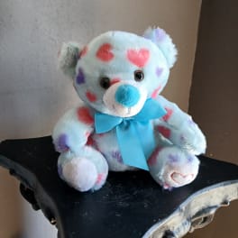 Plush teddy bear with heart patterns and a blue ribbon