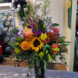 Mixed bouquet in a black vase with sunflowers, roses, lilies, and colorful blooms