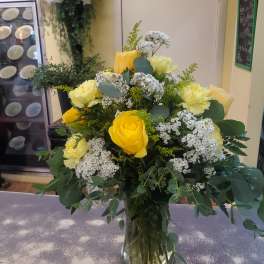Yellow roses and pale carnations in a glass vase with white filler flowers.