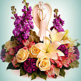 Floral arrangement with lilies, roses, and purple blooms around an angel figurine
