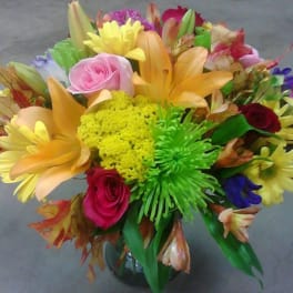 Colorful mixed bouquet with roses, lilies, and daisies in a glass vase