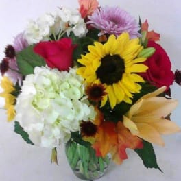 Mixed bouquet with sunflowers, roses, hydrangeas, and lilies in a glass vase