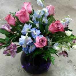 Pink roses and blue flowers arranged in a dark glass vase