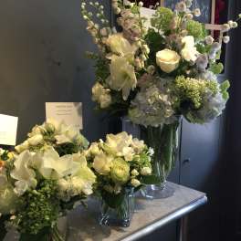 White and pale green floral arrangements in glass vases on a counter