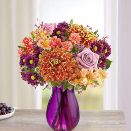 Mixed bouquet of purple, orange, pink, and peach flowers in a purple vase