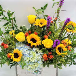 Bright mixed bouquet with sunflowers, yellow roses, and blue hydrangeas in a white box