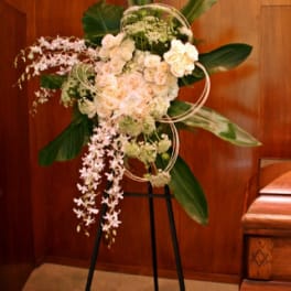 Standing floral spray with pale pink and white blooms on a black easel