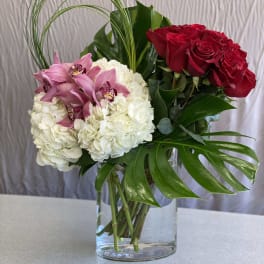 Bouquet of red roses, white hydrangeas, and pink orchids in a glass vase