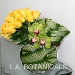 Yellow roses and green orchids in a round glass vase