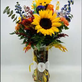 Bouquet with sunflowers, blue flowers, and orange blooms in a clear vase