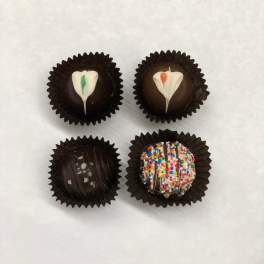 Four decorated chocolate truffles in dark paper cups on a white background