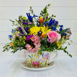Colorful mixed flower arrangement in a floral teacup and saucer with pink, yellow, blue and purple blooms