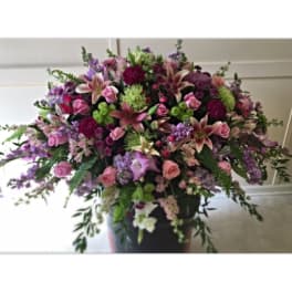 Large mixed bouquet of pink, purple, and green flowers in a dark vase