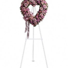 Heart-shaped pink rose funeral wreath on a white stand