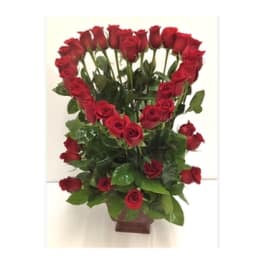 Tall arrangement of red roses shaped into a heart above more roses in a brown vase