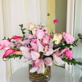 Pink and white flowers arranged in a glass vase with a ribbon