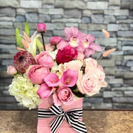 Pink floral arrangement in a pink box with a striped ribbon