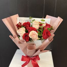 Bouquet of red and blush roses wrapped in pink paper with a red ribbon