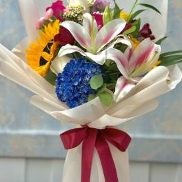 Mixed bouquet with lilies, sunflowers, roses, and hydrangea wrapped in white paper
