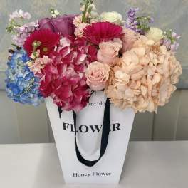 Mixed bouquet of hydrangeas, roses, and gerbera daisies in a white gift bag