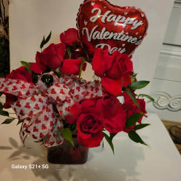Red roses in a vase with a heart-shaped Valentine balloon and heart ribbon