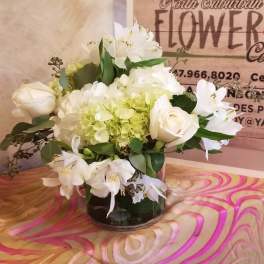 White roses and lilies arranged in a glass vase with pale green hydrangea.