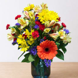 Mixed bouquet in a blue glass vase with orange, yellow, red, and purple flowers