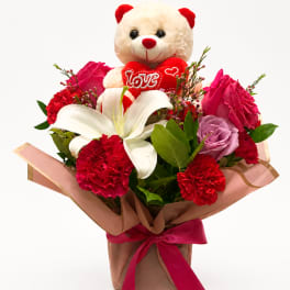 Bouquet with a teddy bear and red and pink flowers in brown wrapping