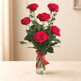 Tall bouquet of red roses in a clear glass vase with a red ribbon