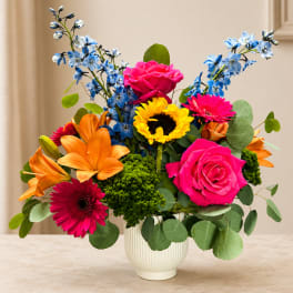 Bright mixed bouquet in a white vase with pink roses, orange lilies, and blue flowers
