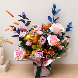 Mixed bouquet of pink, orange, yellow, and blue flowers in a wrapped container