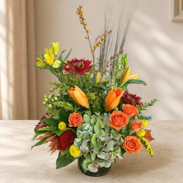 Mixed bouquet in a glass vase with orange roses, lilies, and red blooms