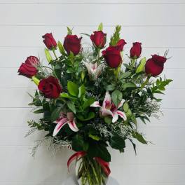 Tall bouquet of red roses and pink lilies in a clear glass vase
