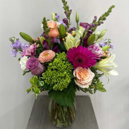 Mixed bouquet in a glass vase with roses, lilies, and purple blooms