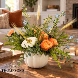 Orange roses and blue flowers arranged in a white pumpkin vase