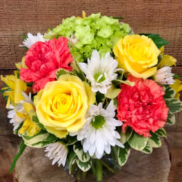 Bouquet of yellow roses, red carnations, white daisies, and green hydrangea in a glass vase