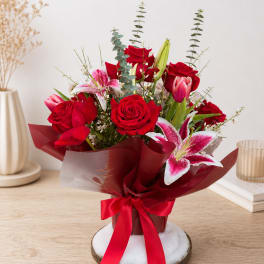 Red roses and pink lilies in a wrapped gift bouquet with a ribbon