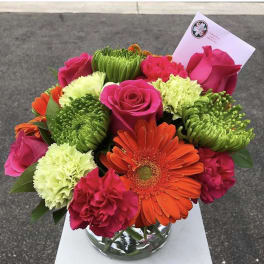 Bright mixed bouquet of roses, gerbera daisies, and carnations in a glass vase