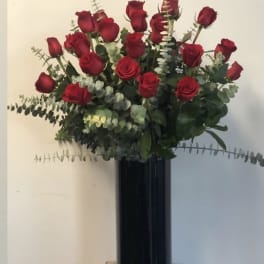 Red roses arranged in a tall black vase with eucalyptus